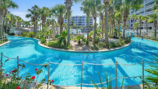 Una piscina rodeada de palmeras y un edificio de varios pisos con balcones.