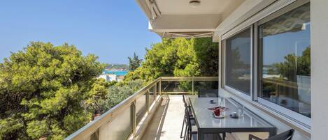 A balcony with a table and chairs, overlooking a lush green landscape and a clear blue sky.