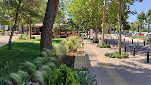 Un espace urbain aménagé avec un café, une allée pavée et un parking où sont garées des voitures.