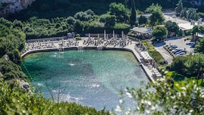 Une station balnéaire dotée d’une piscine entourée de chaises longues et de parasols, d’un parking et d’une végétation luxuriante.