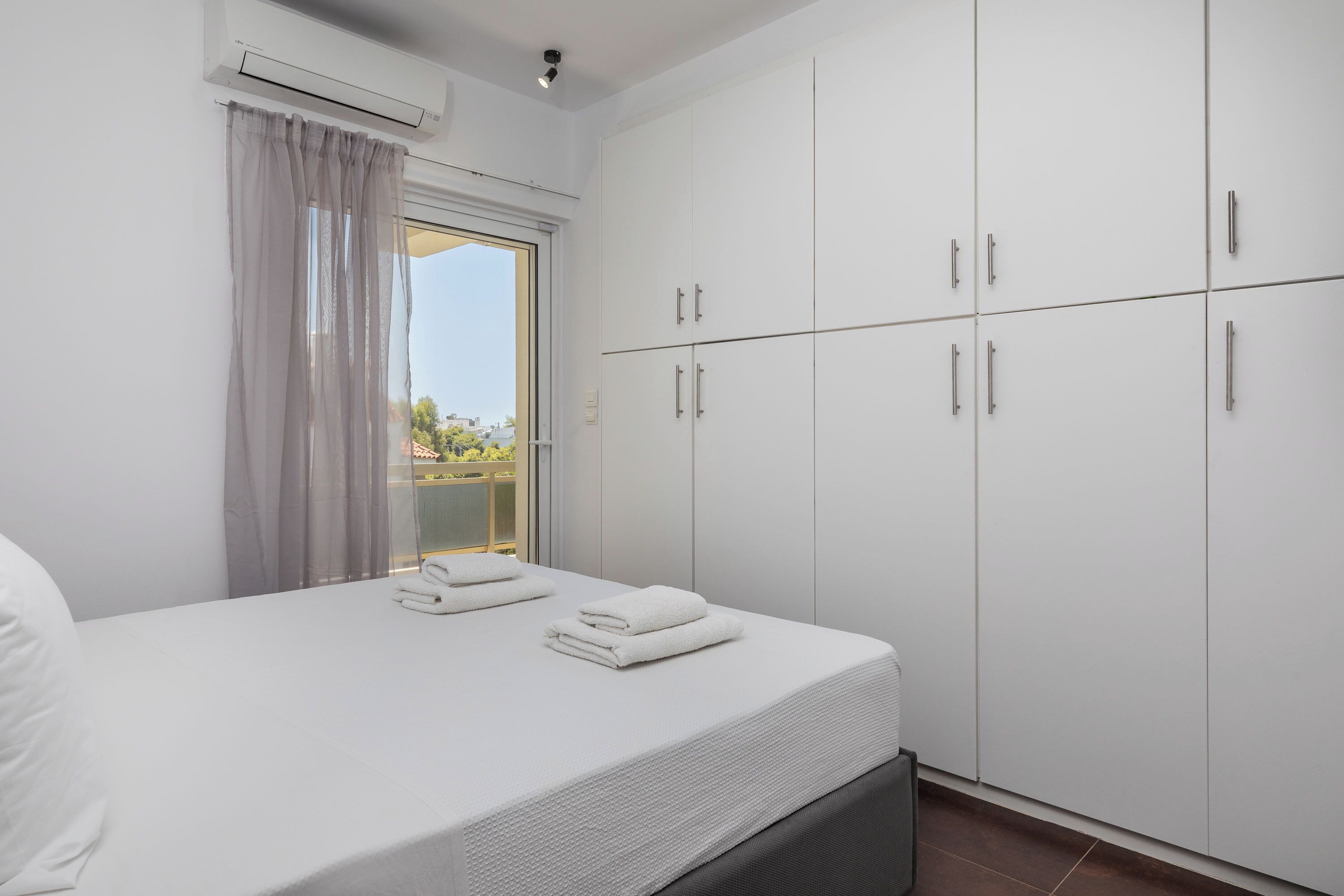 Un dormitorio con cama, cortinas blancas, una ventana y un armario.