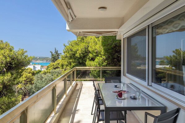 Un balcon avec une table et des chaises, offrant une vue panoramique sur des arbres et une étendue d’eau.