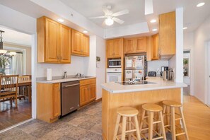 Cozinha moderna com armários de madeira, uma ilha central com banquetas, lava-louças, micro-ondas e geladeira.