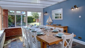 Un comedor con mesa de madera dispuesta para seis personas, sillas blancas y una decoración de velero en la pared.