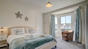 Un dormitorio con una cama grande, una mesita de noche, una silla y una ventana con cortinas.
