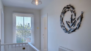 Un pasillo con barandilla blanca, un radiador y una decoración de peces metálicos en la pared.
