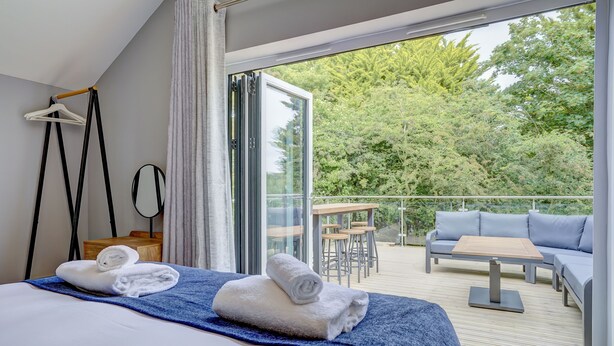 Ein Hotelzimmer mit Bett, Balkon mit Sofa und Tisch sowie Blick auf Bäume.