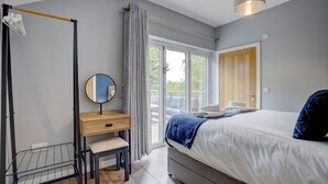 Ein modernes Schlafzimmer mit Bett, Schreibtisch, Stuhl, Kleiderhaken und einer Glastür, die zu einem Außenbereich führt.