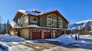 Une grande maison à deux étages, avec des fondations en pierre, plusieurs portes de garage et une allée recouverte de neige.