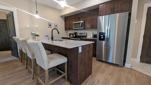 Une cuisine moderne dotée d’un îlot central, d’appareils électroménagers en acier inoxydable, de meubles en bois et de tabourets de bar.
