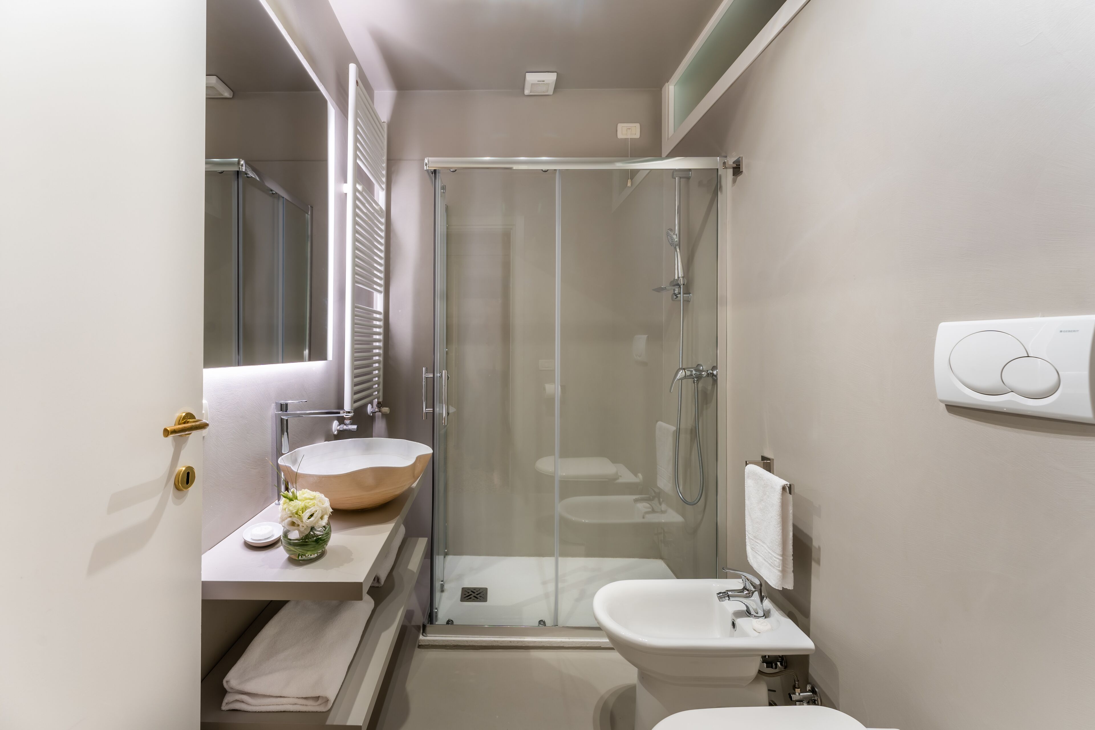 A compact bathroom with a glass-enclosed shower, a wooden bowl sink, and a white pedestal sink.
