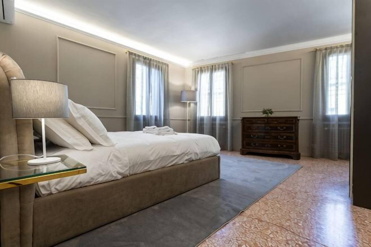 Ein Schlafzimmer mit Bett, Nachttischen, einem Schminktisch und einem Fenster mit Vorhängen.