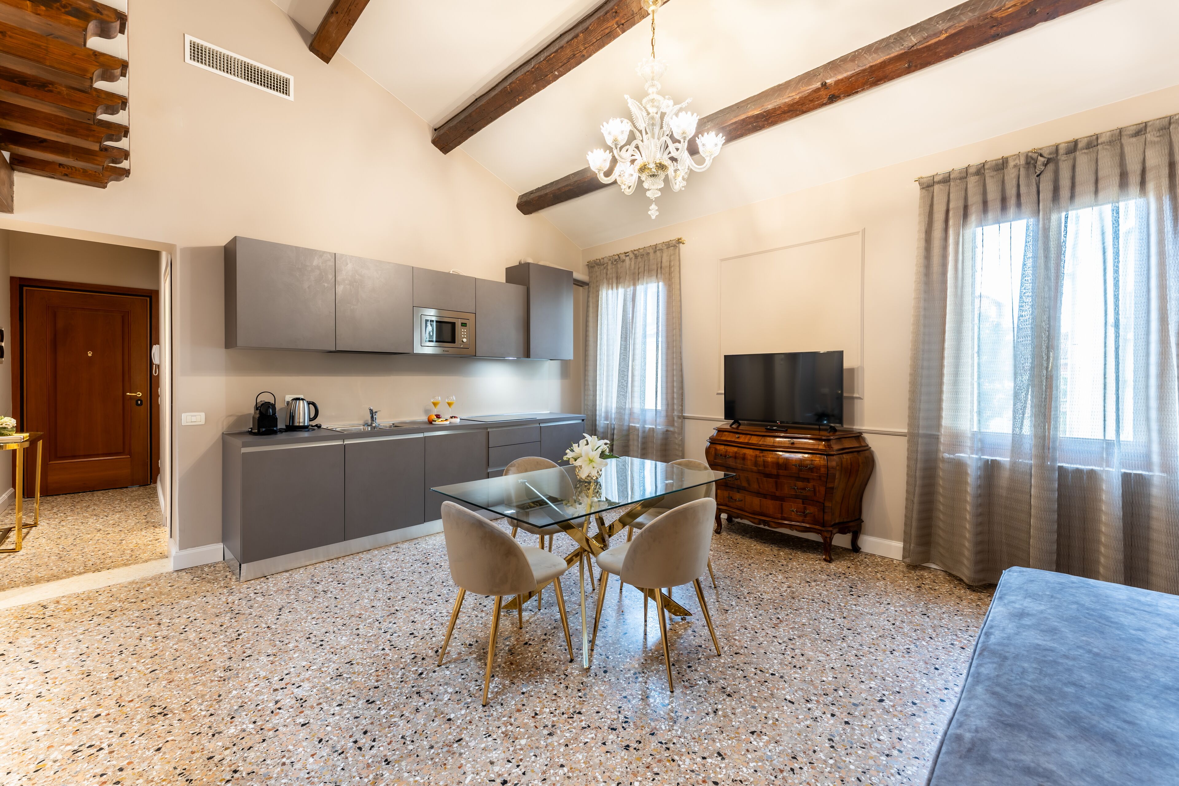 Una cocina moderna con armarios grises, un microondas y un comedor con una mesa de vidrio y cuatro sillas.