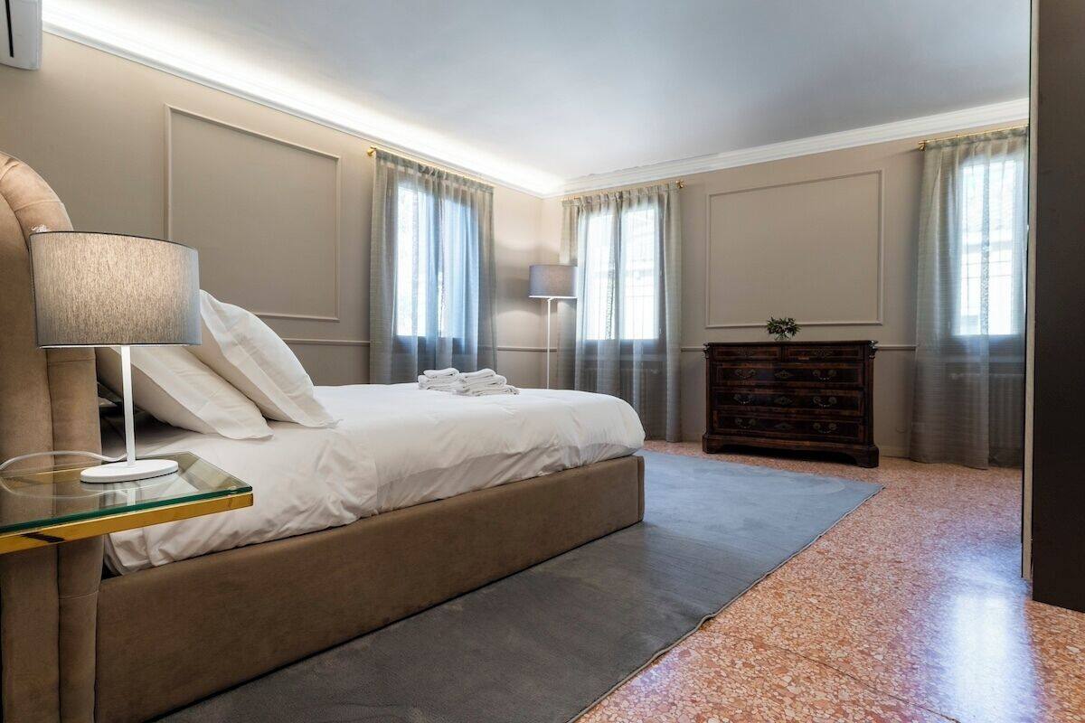 Ein modernes Hotelzimmer mit einem großen Bett, einem Glastische, einer Lampe und einer Holzkommode.