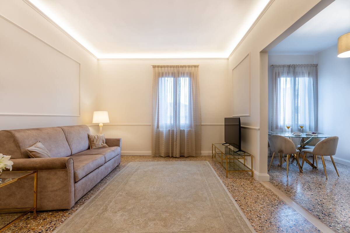 Ein Wohnzimmer mit Sofa, Fernseher und Essbereich mit Stühlen und Tisch.