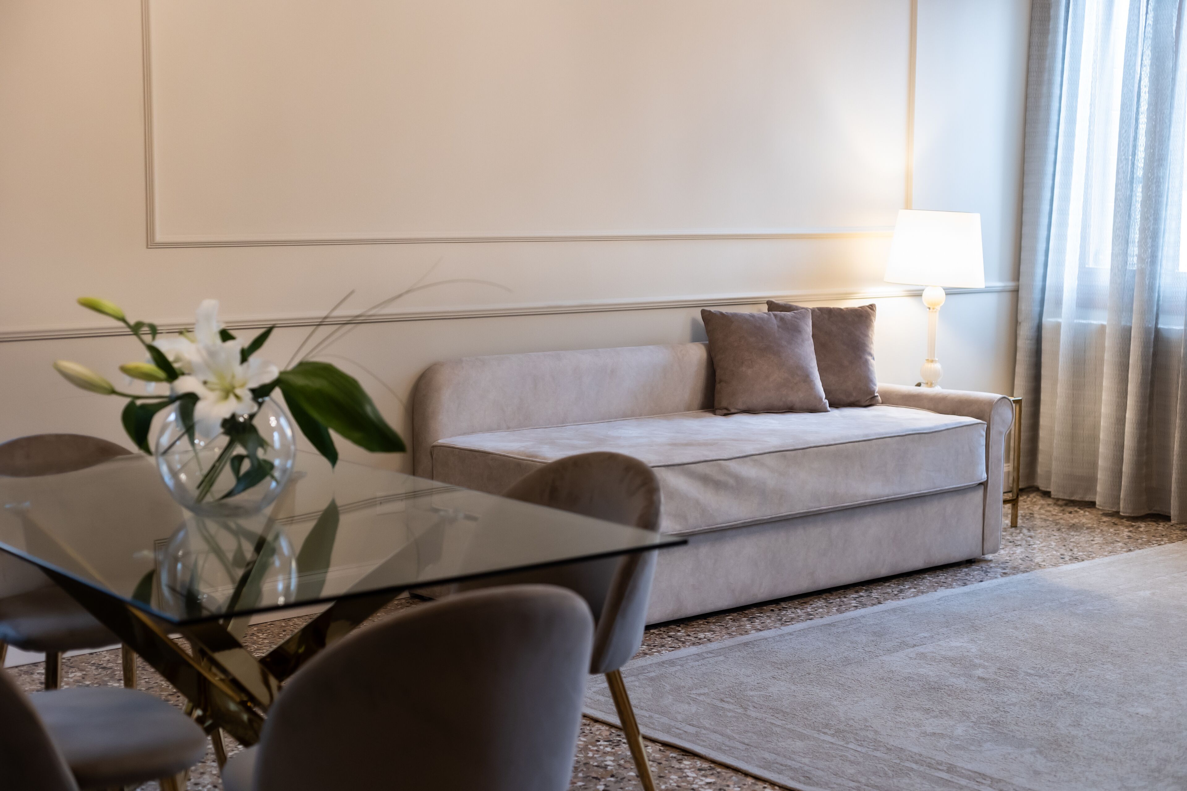 Una sala de estar moderna con una mesa de centro de vidrio, un sofá color beige y una lámpara.