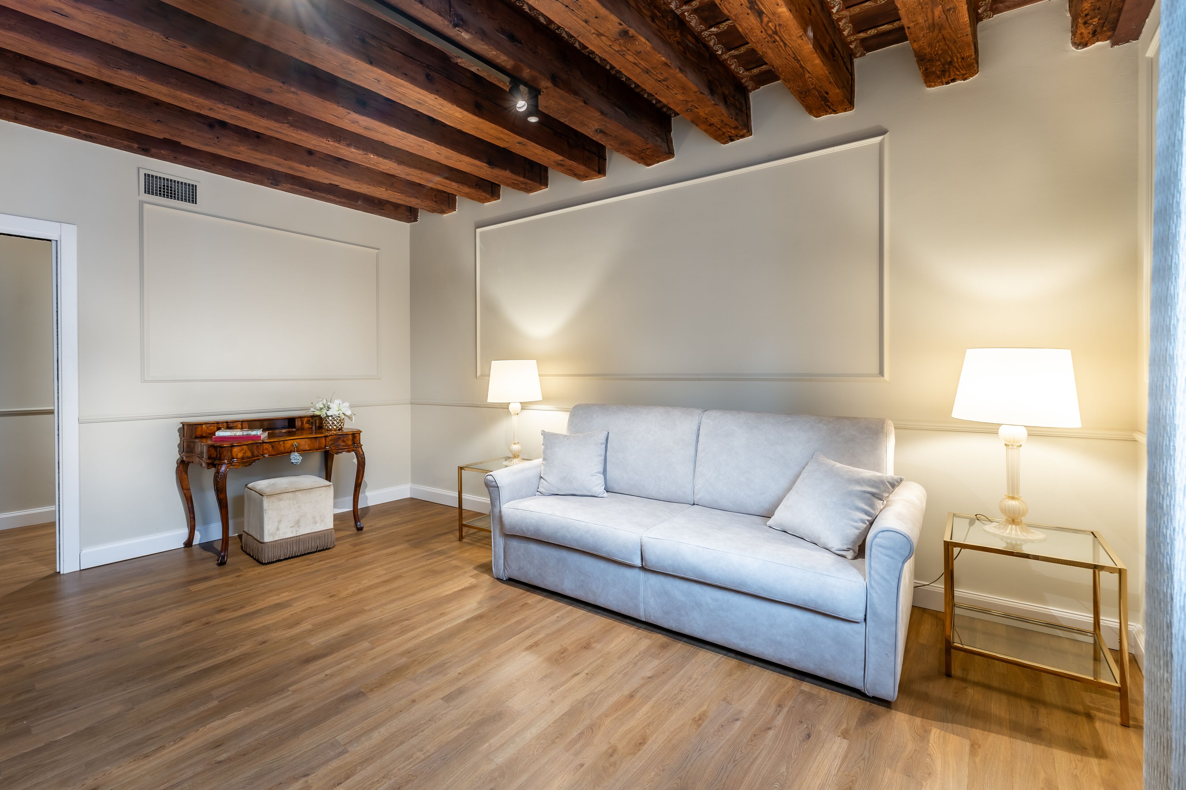 A room with a light grey sofa, wooden flooring, a wooden ceiling, and two bedside lamps.