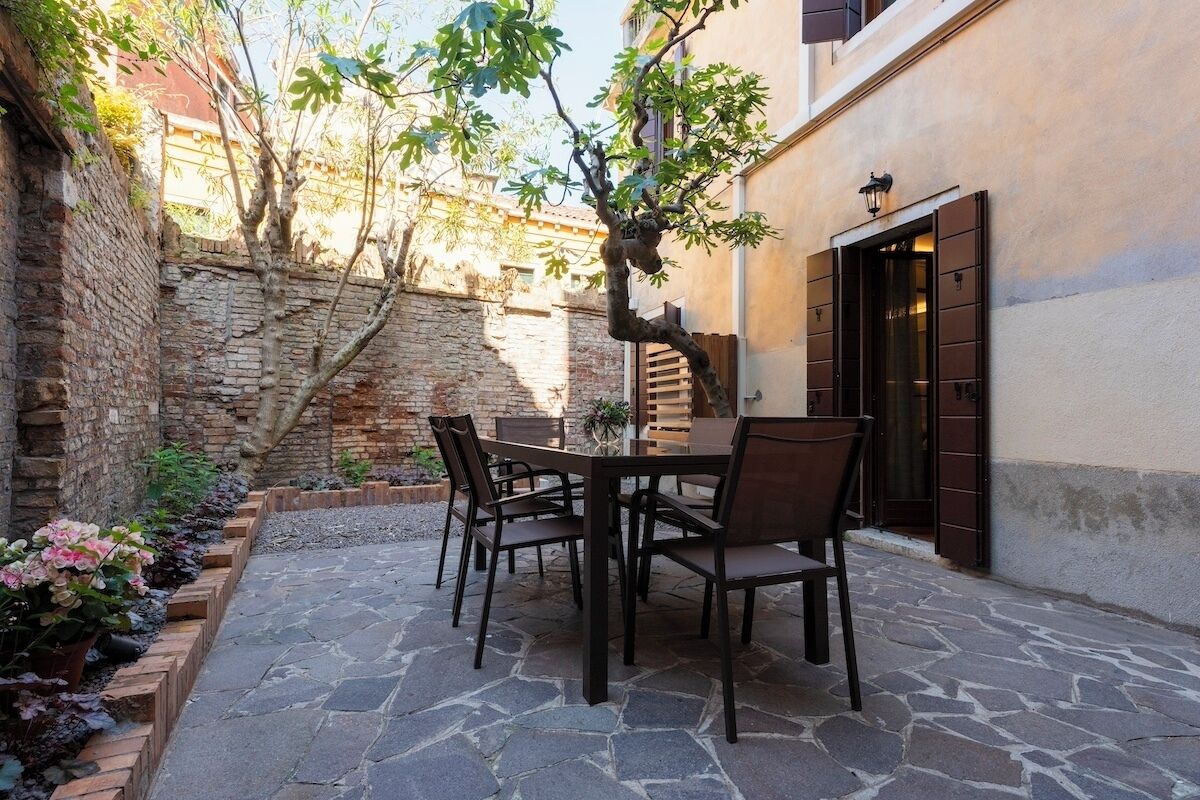 An outdoor patio with stone flooring, a wooden table, and chairs.