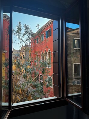 A view through a window of a building with a red facade, a balcony, and some greenery. - SAN VIO PALACE LUXURY APARTMENTS (Venice)