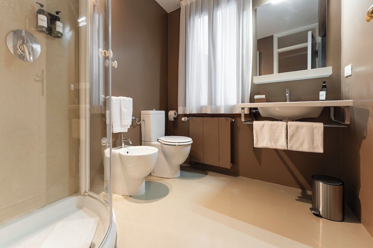 A modern bathroom with a glass-enclosed shower, two toilets, a sink, and a mirror.