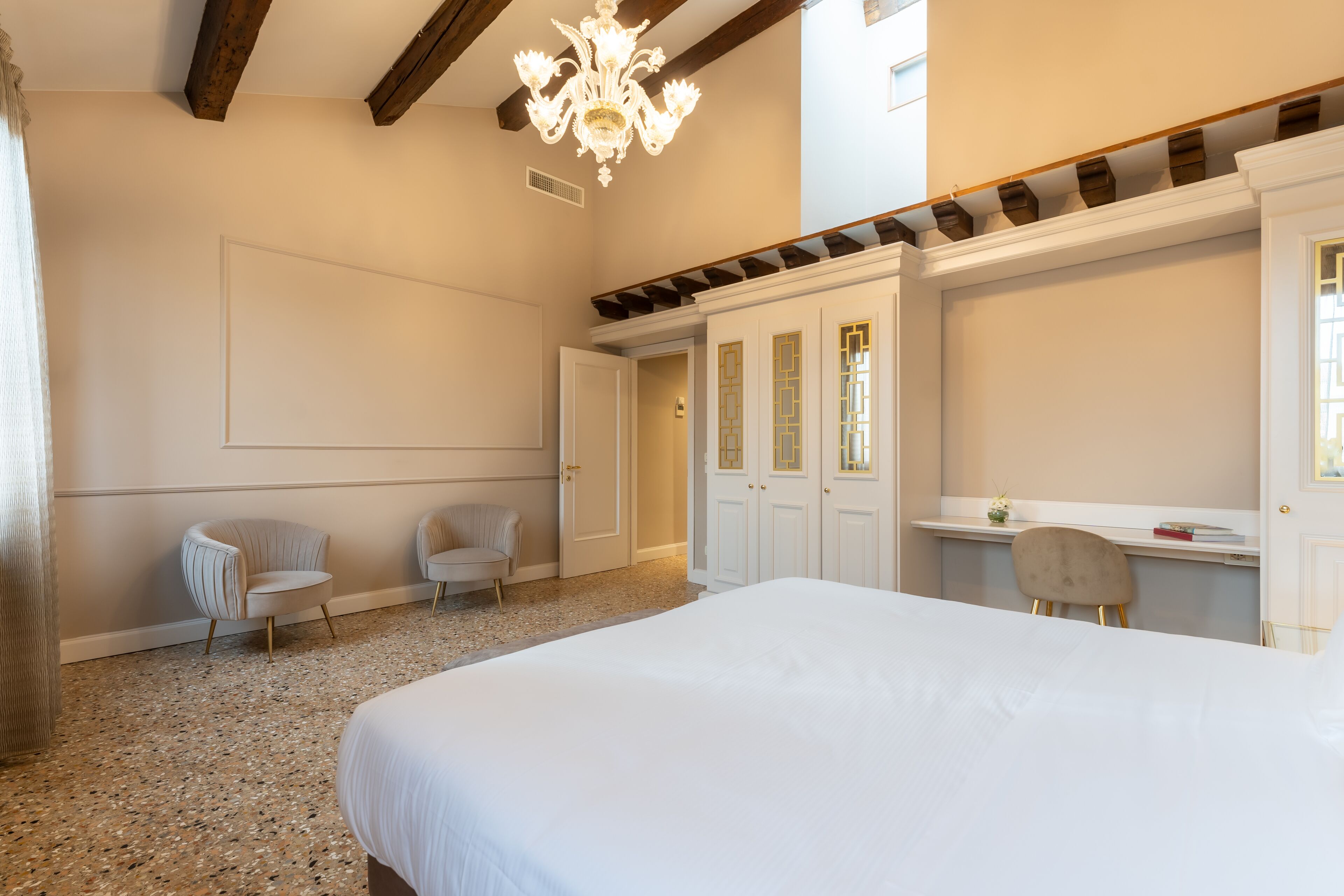 A bedroom with a large bed, two chairs, a desk, and a chandelier.
