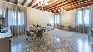 A modern living room with a dining area, wooden ceiling beams, and a chandelier. - SAN VIO PALACE LUXURY APARTMENTS (Venice)