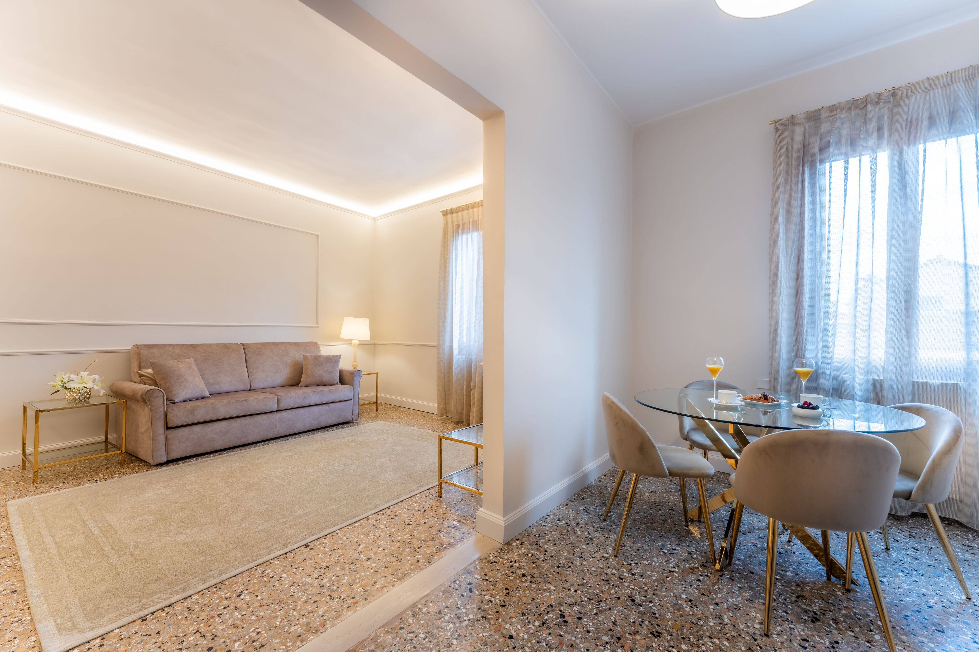 A modern living room with a sofa, a glass coffee table, and a dining area with chairs and a table.