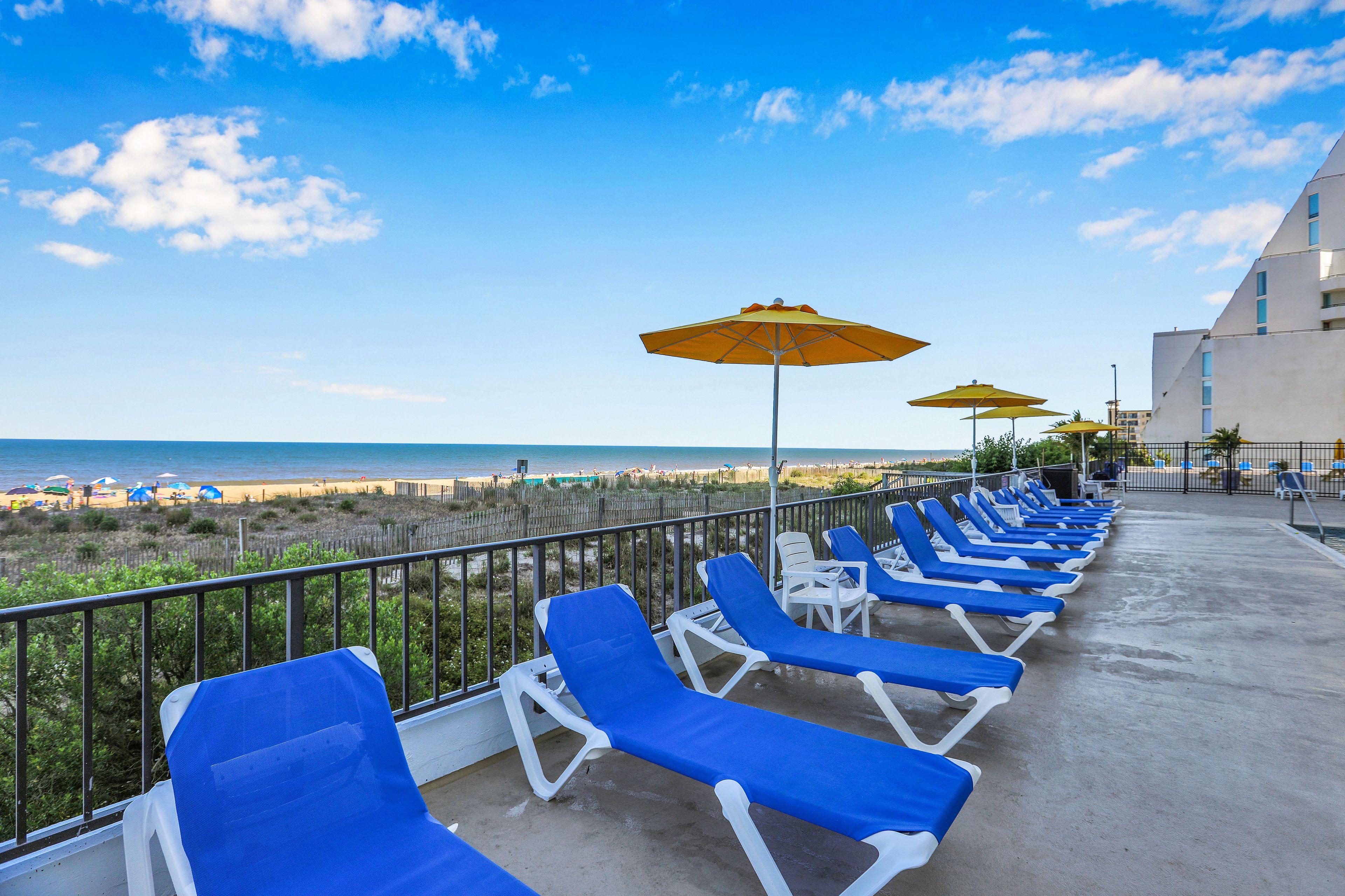 A balcony with blue lounge chairs and yellow umbrellas overlooking a beach.