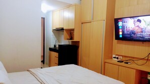 A hotel room with a bed, a TV mounted on the wall, a small kitchenette, and wooden cabinets. - Transpark Juanda Bekasi by 21 Room (Bekasi)