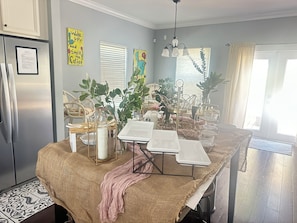 Cozinha com mesa de jantar, cadeiras, geladeira e janela com persianas.