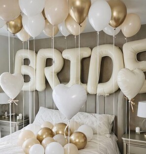 En seng pyntet med hvide og gyldne balloner, der staver 'BRIDE', samt hjerteformede balloner.