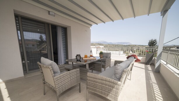 Ein Balkon mit Korbmöbeln, einem Tisch und Blick auf ferne Berge.