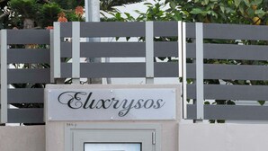 Ein begrenzter Eingangsbereich mit einem Schild, auf dem "Elxrysos" steht, und einem gerahmten Bild von gelben Blumen.