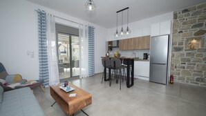 Eine moderne Wohnung mit Wohnzimmer, Küche und Essbereich. Es gibt ein Sofa, einen Holztisch und einen Esstisch mit Stühlen. Die Küche verfügt über Holzschränke und einen Edelstahlkühlschrank.
