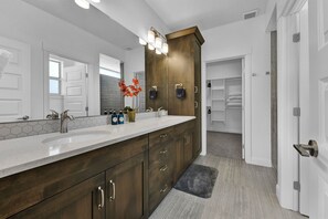A modern bathroom with a large mirror, wooden vanity, and a walk-in closet.