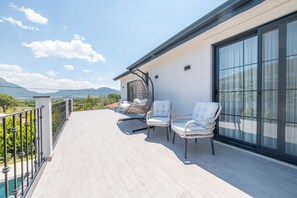 A balcony with two white cushioned chairs, a hanging chair, and a glass door.