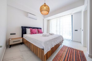 A modern bedroom with a bed, bedside tables, a hanging light fixture, and a view of the outside.