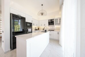 A modern kitchen with white cabinetry, a central island, stainless steel appliances, and a pendant light.