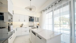 A modern kitchen with white cabinetry, a marble floor, and a large window with a view. - Misty Mountain Luxury Villa Fethiye, Uzumlu (Fethiye)