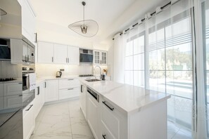 Een moderne keuken met witte kastjes, een marmeren vloer en een groot raam met uitzicht.
