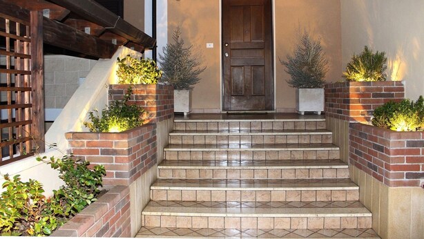 A set of stone steps leading to a wooden door, flanked by brick planters with small shrubs.