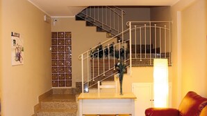 A staircase with metal railings leading to a landing, a white table, and a red leather sofa in a well-lit room with beige walls.