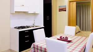 A compact kitchen with a gas stove, a sink, and white cabinets. There is a dining area with a table set for two, covered by a checkered tablecloth.