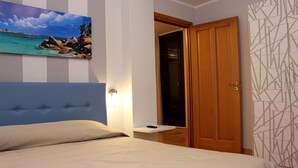 A bedroom with a bed, a painting of a beach scene, a wooden door, and a patterned wall.