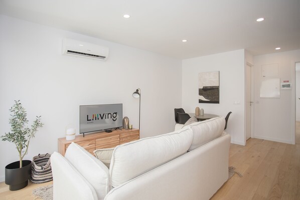 A modern living room with a white sofa, a flat-screen TV, a potted plant, and a wooden cabinet. - NAX Apartment E by Liiiving (Porto)