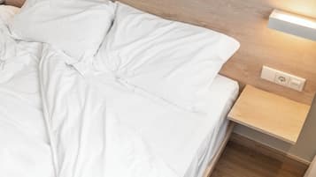 Una cama bien hecha con ropa blanca, un cabecero de madera y una mesita de noche con interruptor de luz.