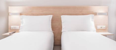 Una cama doble con cabecera de madera, ropa de cama blanca y mesitas de noche con lámparas.