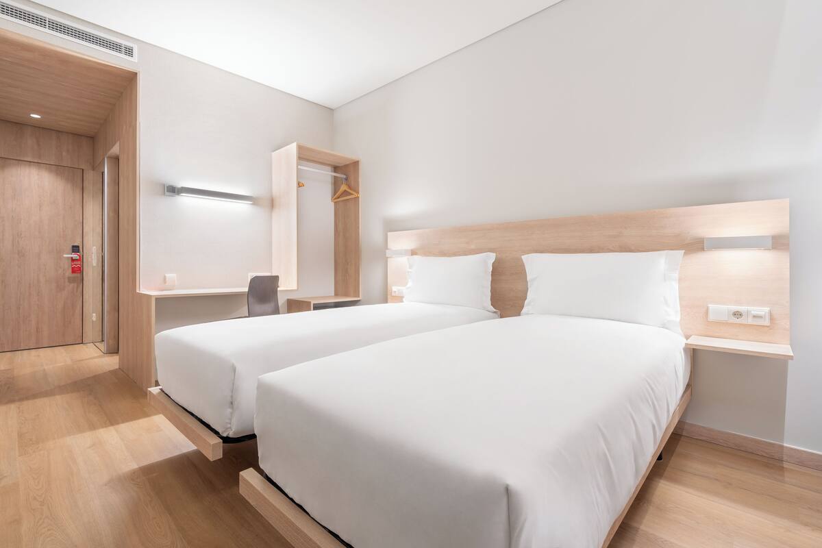 Une chambre d’hôtel moderne équipée de deux lits, d’un bureau et d’une armoire.