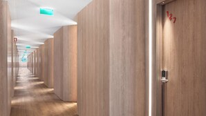 Corredor moderno de hotel com lambris de madeira, um longo hall e uma porta com fechadura eletrônica.