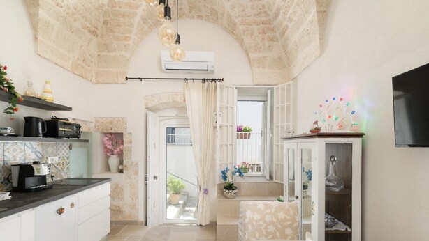 A kitchen with a stone wall, a dining area with a white table, and a TV mounted on the wall.